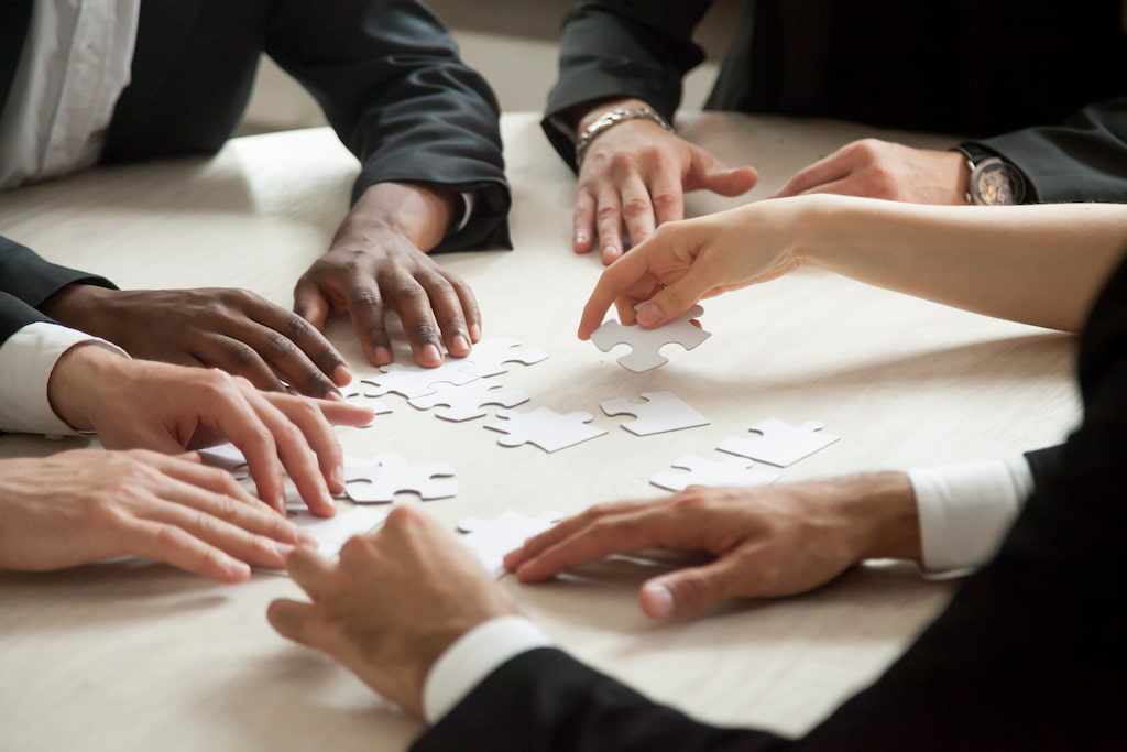 image of 4 pairs of hands on a table assemblying a puzzle, evoking the feeling of making effective decisions