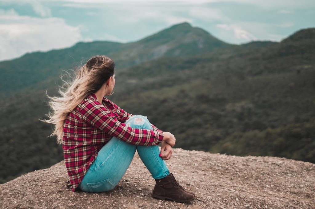 thoughtful woman sitting on a rock watching mountains