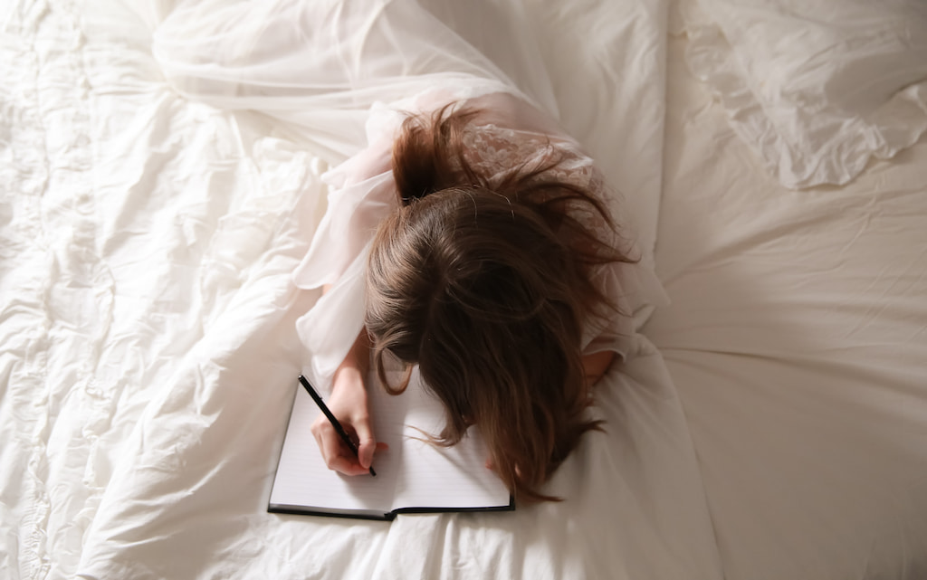 
woman writing a gratitude journal in bed