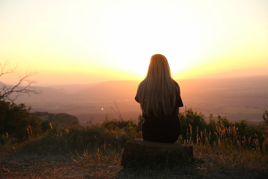 young woman sitting on a rock and looking at view