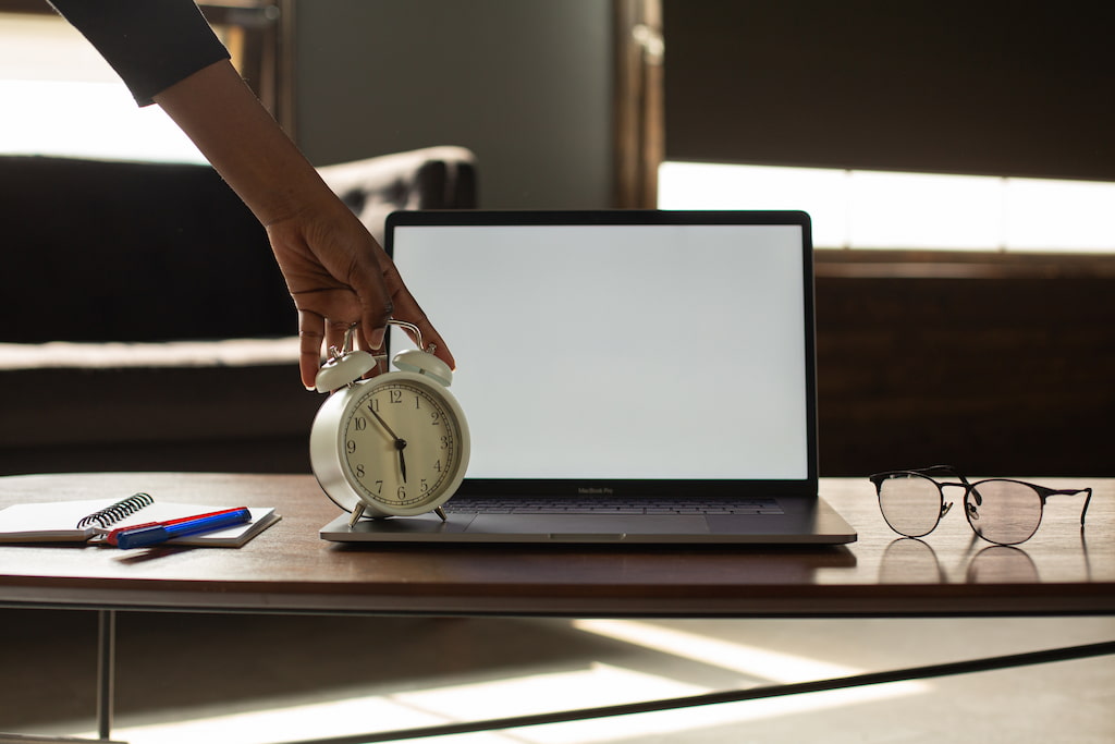 image of a clock in front of a laptop, evoking the action of procrastinating at work