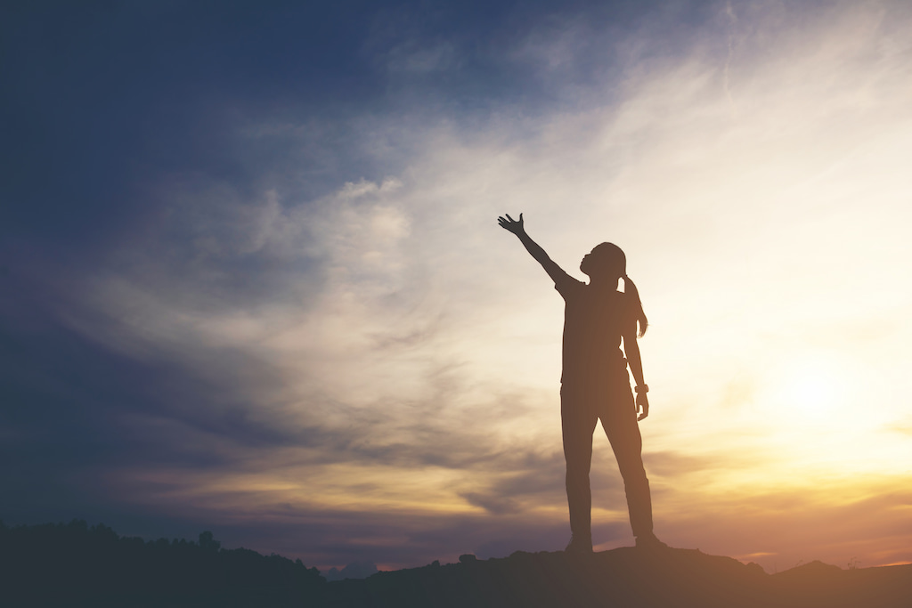 image of a person on a mountain, extending their arm like reaching for the sky, evoking the sense of unlocking their inner resources